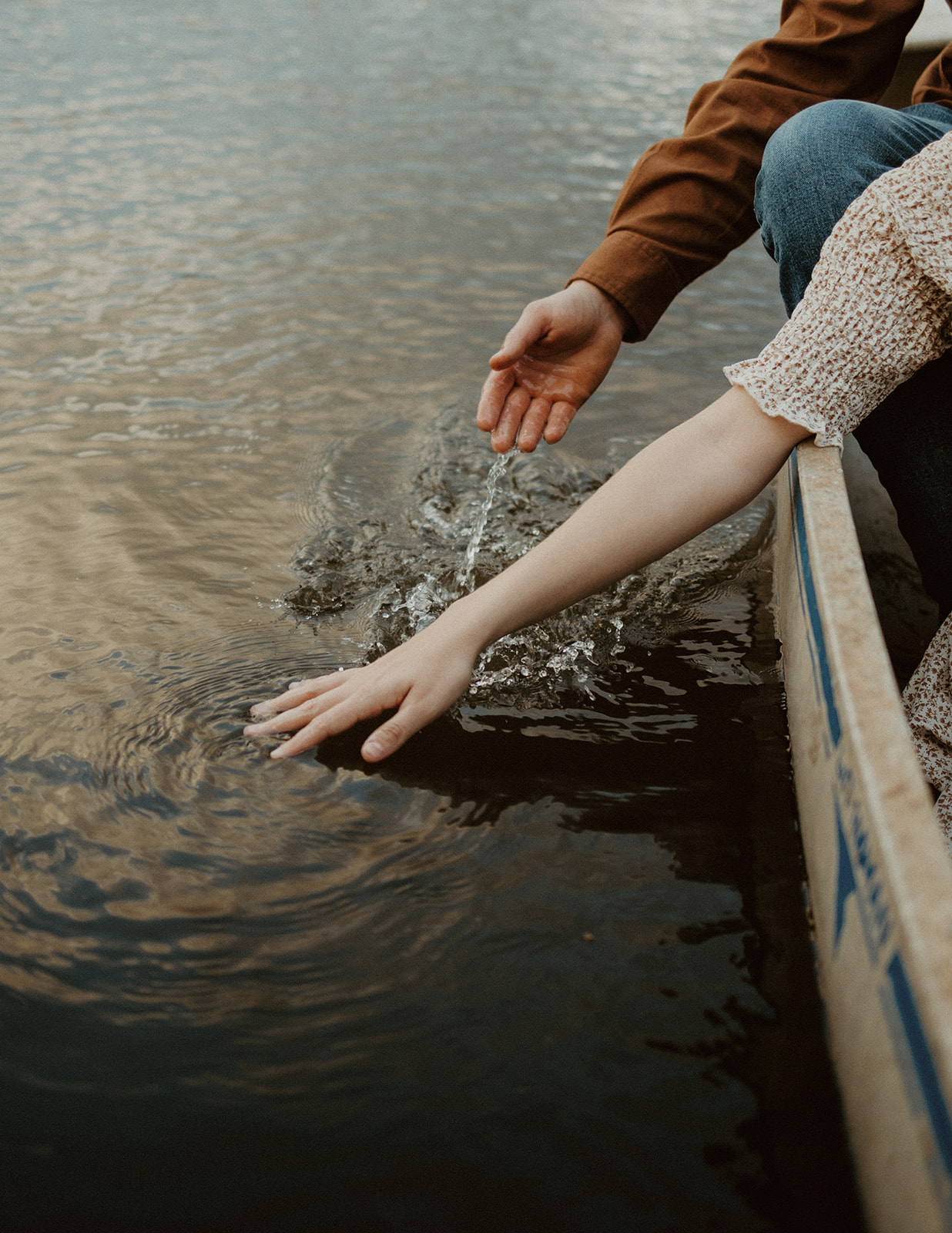 the couples hands gently touch the lake water as they float in their canoe