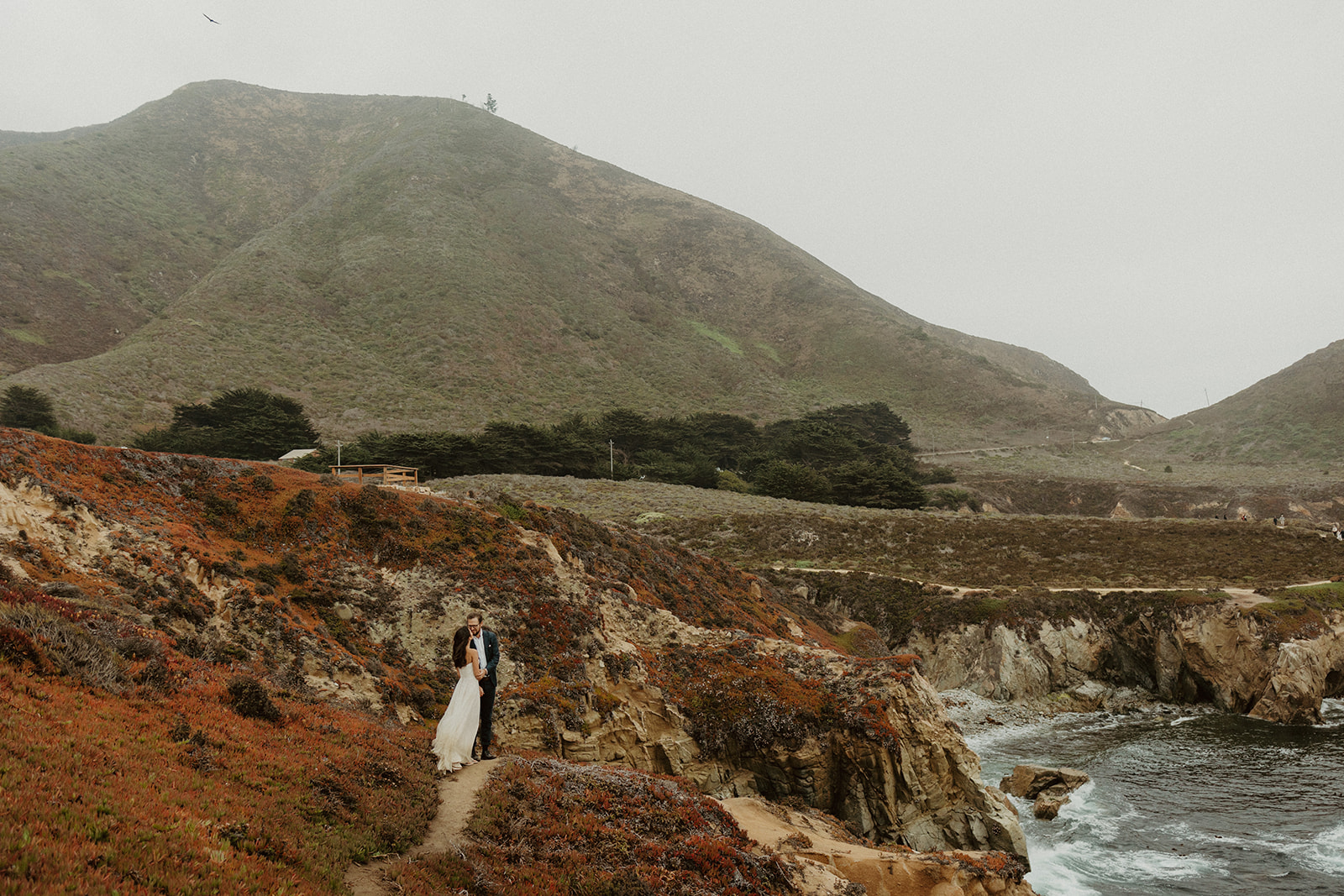 the couple standing together at the edge of the coast during their foggy elopement in Big Sur