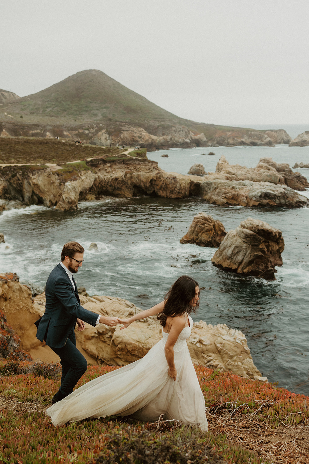 the bride and groom walking along the coast at their foggy elopement in Big Sur