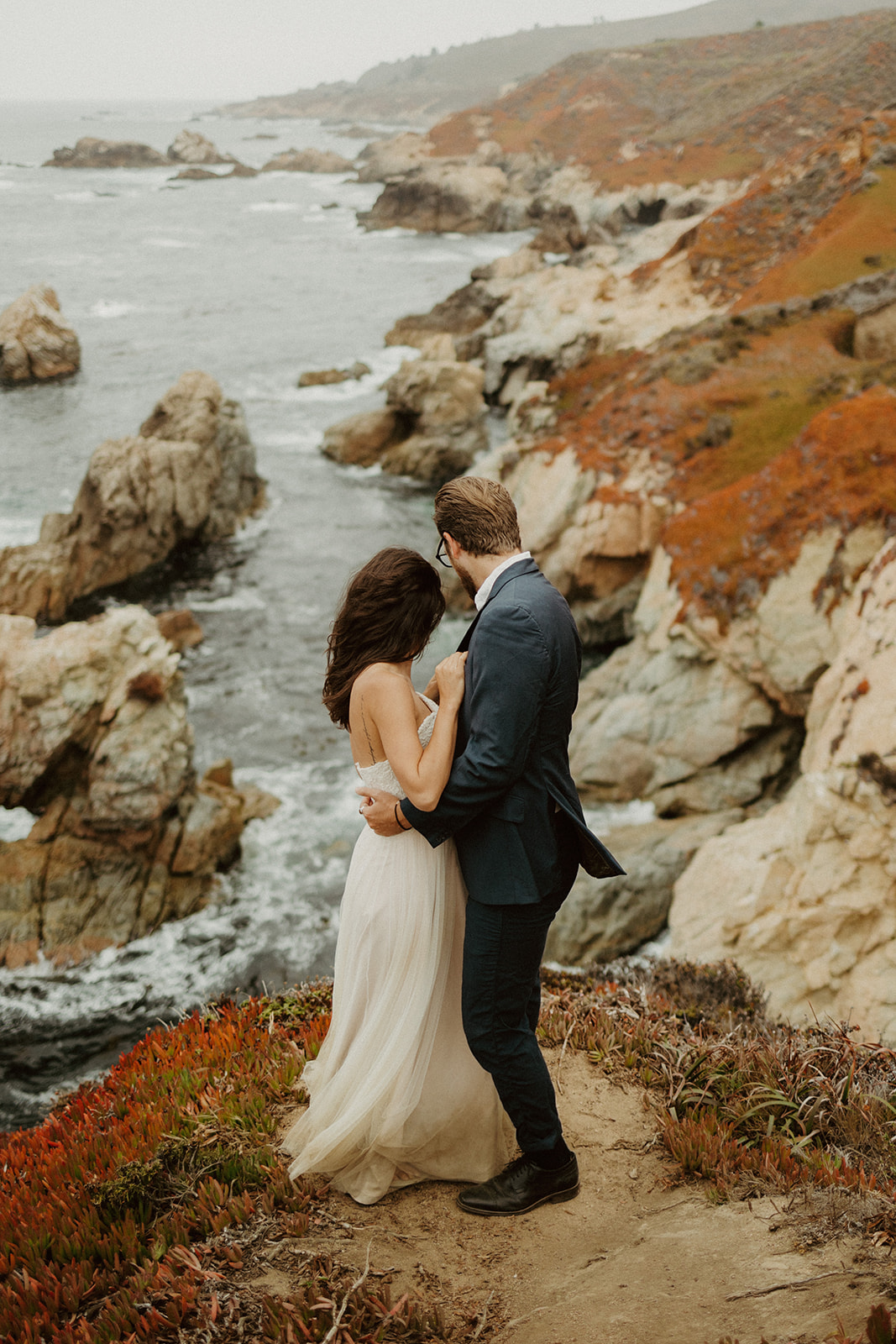 the couple standing together and looking down at the water and rocks below