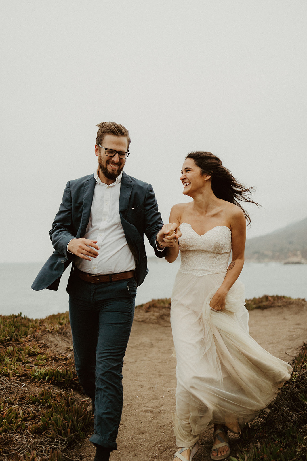the couple laughing and walking as the wind blows their hair