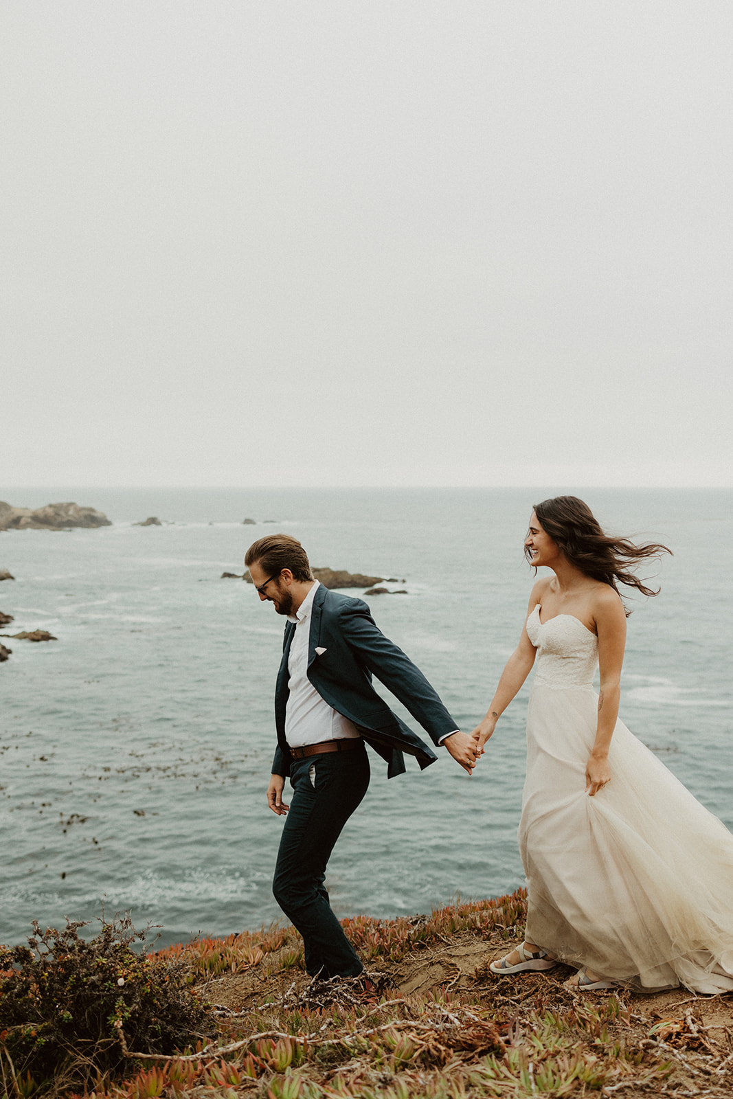 the couple holding hands as they walk down the coast