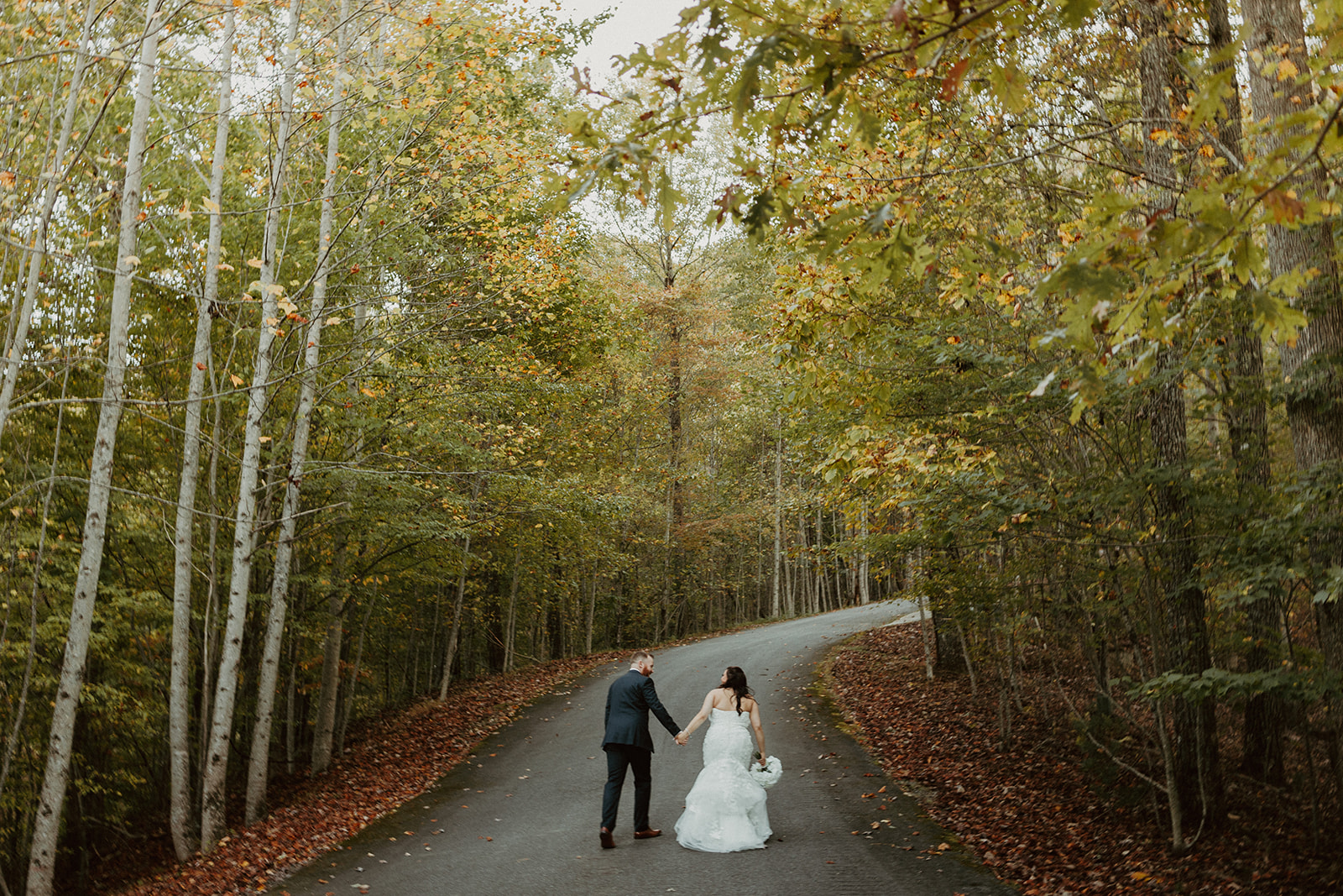 couple walking down the road under the fall trees at the airbnb wedding venue
