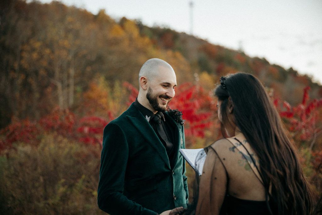 the groom smiling at the bride while she says her vows for their mountain elopement